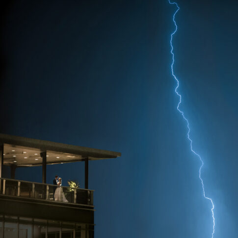 Newly married couple embraces on the balcony of their wedding reception in Greenville SC during a lightning storm.