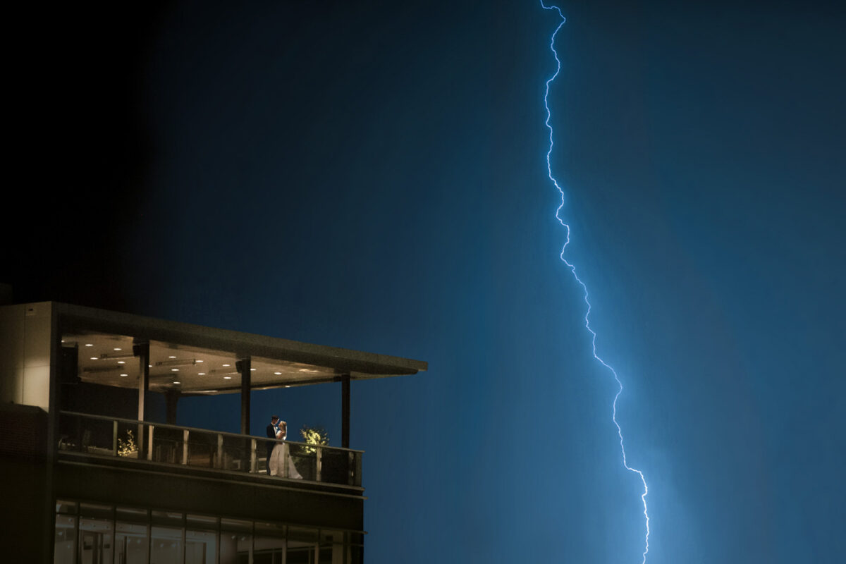 Newly married couple embraces on the balcony of their wedding reception in Greenville SC during a lightning storm.