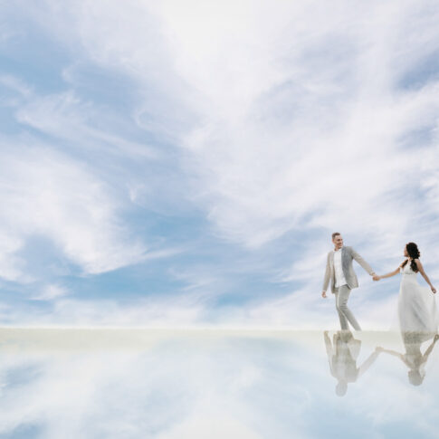 Newlyweds hold hands and walk through a sky filled with clouds