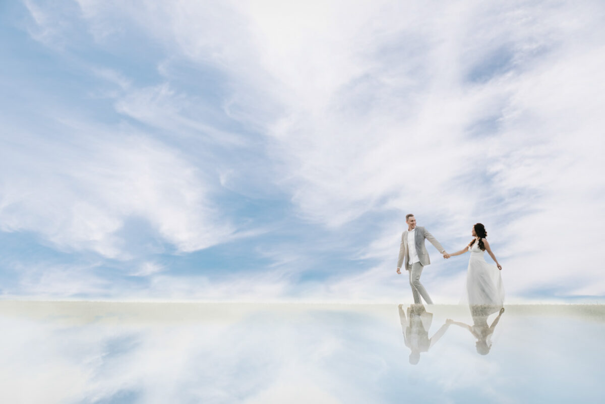 Newlyweds hold hands and walk through a sky filled with clouds