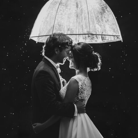 Bride and groom snuggle under an umbrella in the rain.