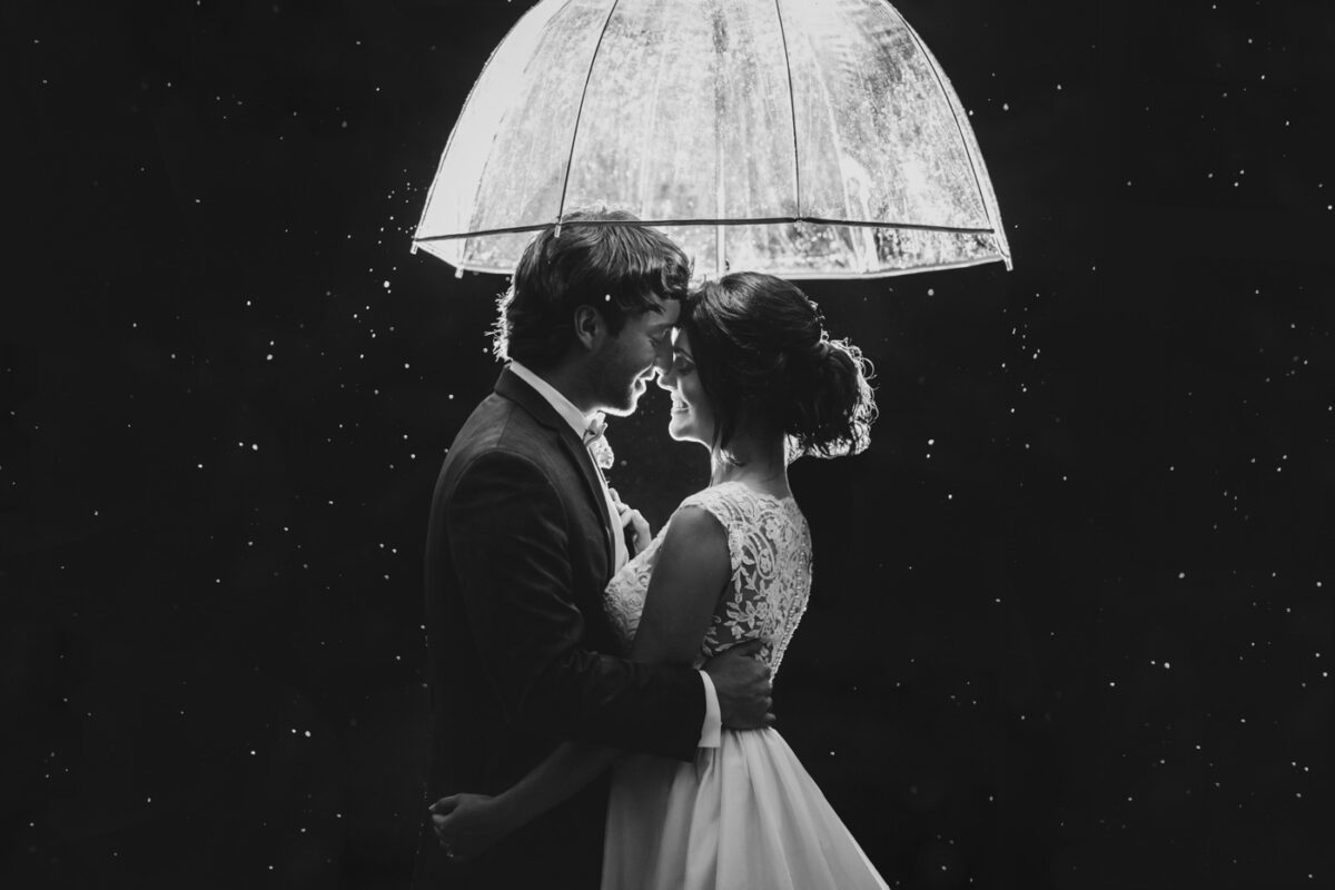 Bride and groom snuggle under an umbrella in the rain.