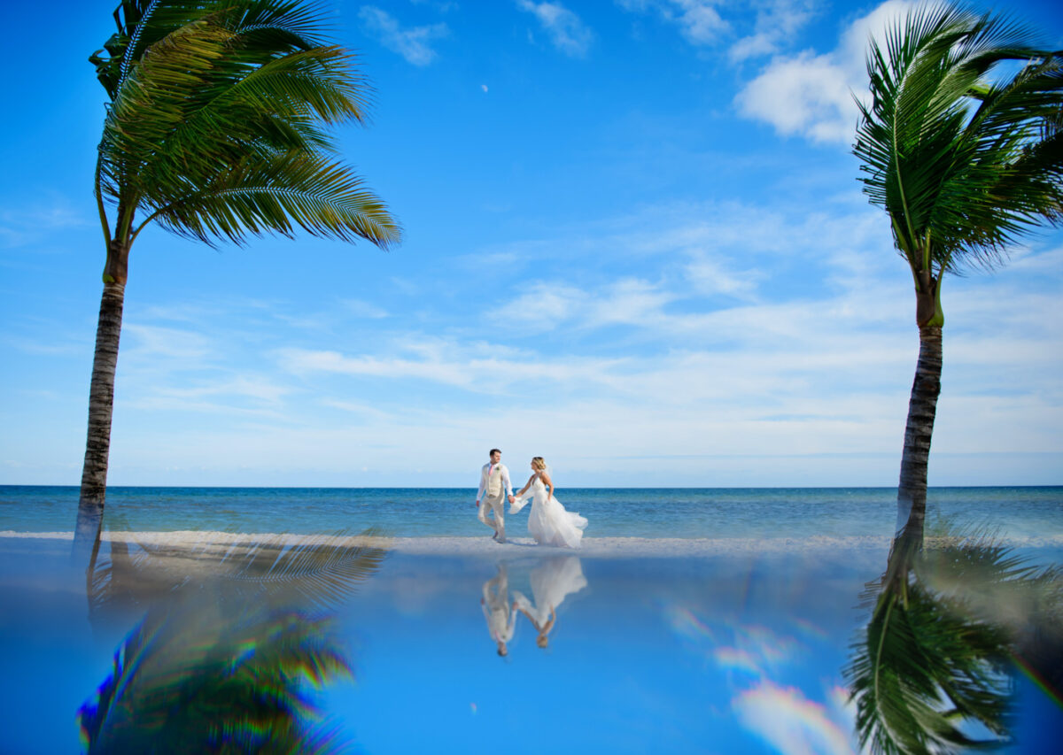 A soon-to-be married couple walks down the beach between two palm trees.