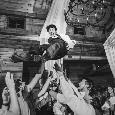 Groomsmen throw the groom high in the air at a reception celebration.