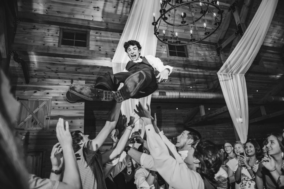 Groomsmen throw the groom high in the air at a reception celebration.