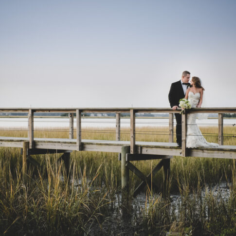 A bride and groom embrace in a stunning sunset overlooking the marsh and river in South Carolina.