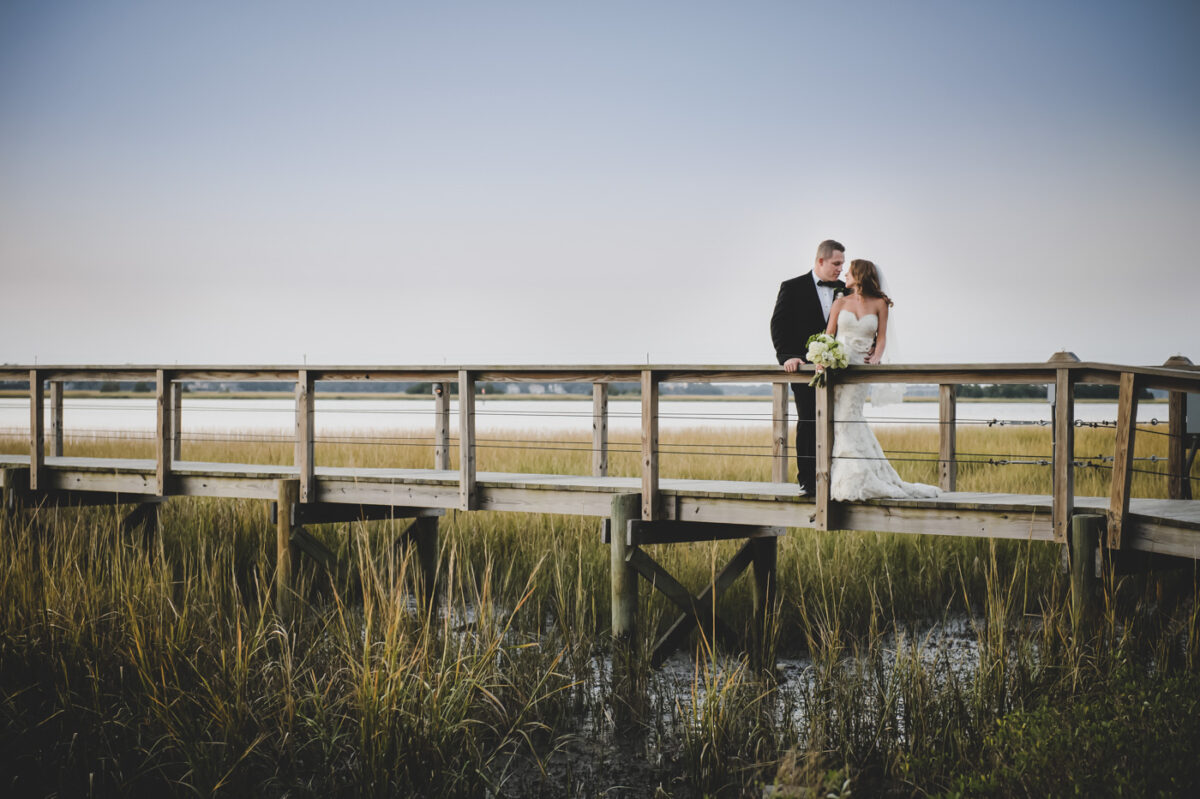 A bride and groom embrace in a stunning sunset overlooking the marsh and river in South Carolina.