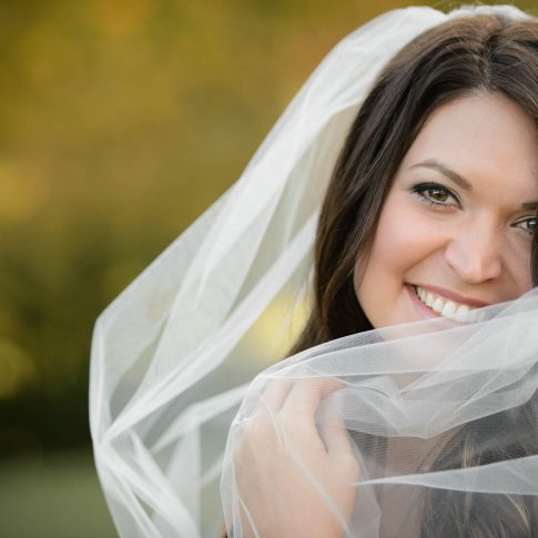 A bride smiles into the camera as she pulls her tulle veil across her.