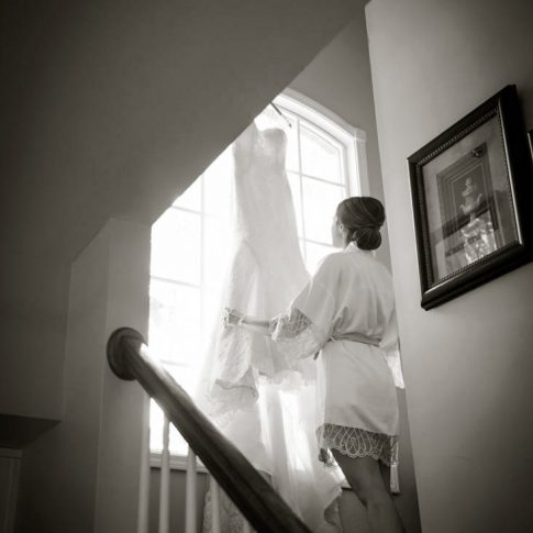 A bride carefully adjusts her wedding gown as it hangs from the windowsill as she is getting ready for her wedding ceremony.