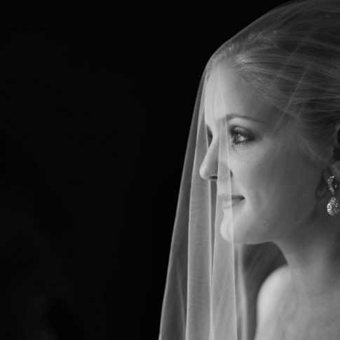 As a tulle bridal veil cascades over the face of the bride, she softly stares into the distance during a bridal photo session.