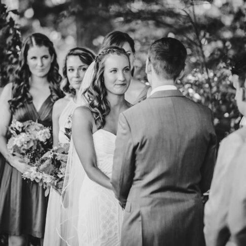 A bride lovingly admires her soon-to-be husband and begins to tear up during an outdoor wedding ceremony.