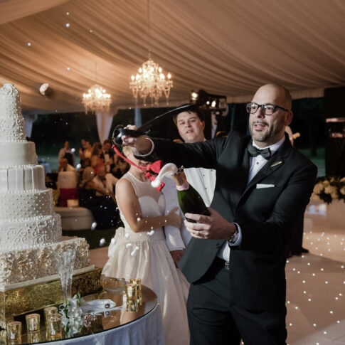 A groomsman expertly pops the bottle of champagne with a saber in preparation for a celebratory toast of the new couple.