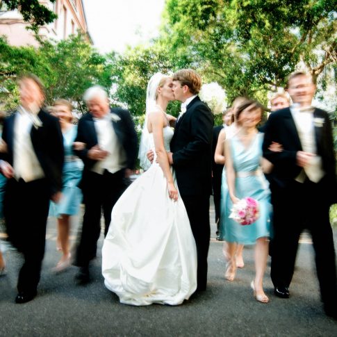 Shot in Charleston, SC the bride and groom pause in the middle of the road for a quick kiss while the rest of the wedding party continues excitedly past them.