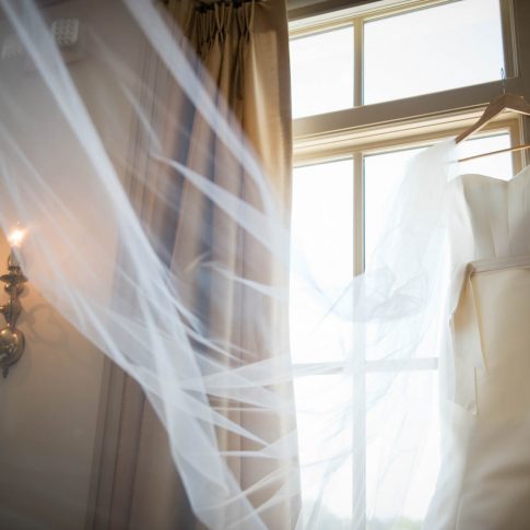 The wedding dress hangs elegantly on the windowsill of the window of the venue, the Charleston Country Club, as the veil gracefully cascades down.