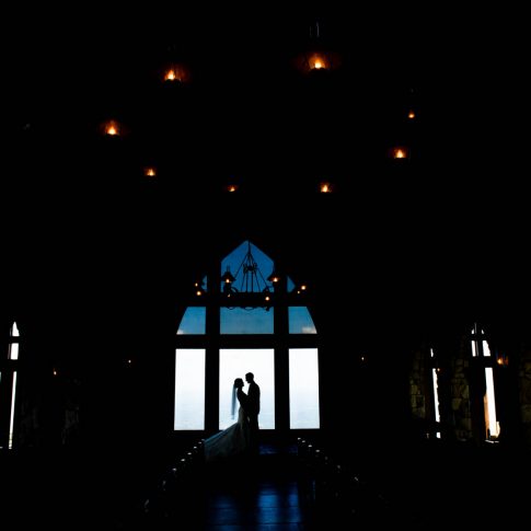 A bride and groom share an intimate gaze in the silhouette of the windows of their venue, The Cliffs at Glassy Chapel.