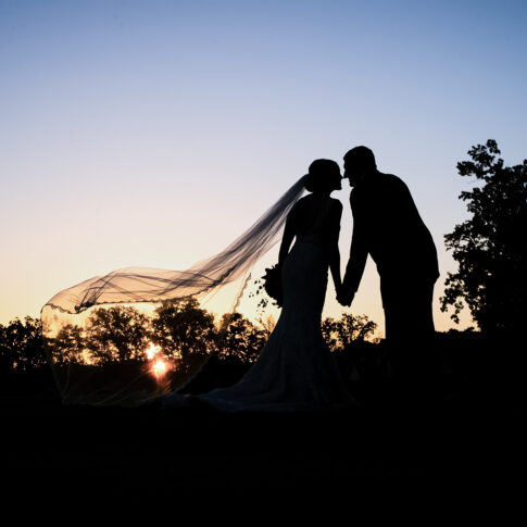 Silhouette photograph of a bride and groom at sunset.