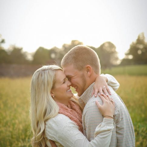 A happily engaged couple lovingly embraces in a sunny field.