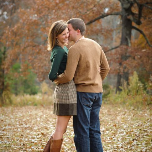 Fiance's happily lean in for a kiss on the cheek as they pose among the fallen fall leaves in Greenville, SC.