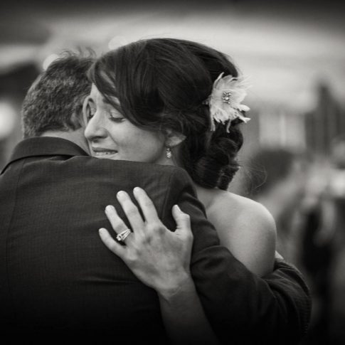 A daughter and father tearfully share a loving embrace on her wedding day.