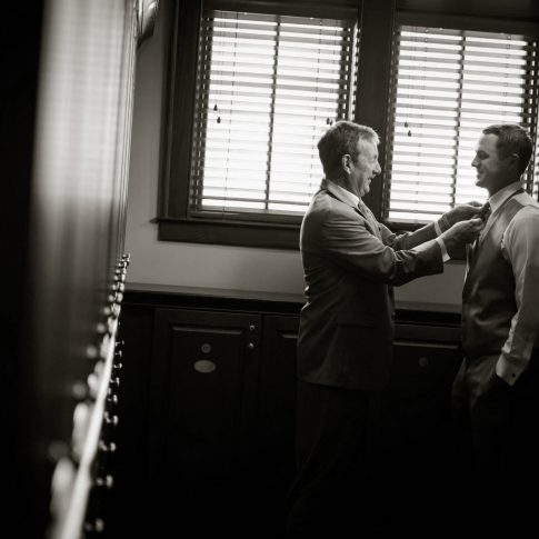 A father carefully adjusts his sons tie as they prepare for his upcoming wedding.