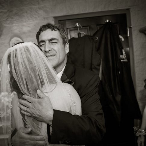 A father embraces his daughter on her wedding day as her mother looks on lovingly to this touching moment.