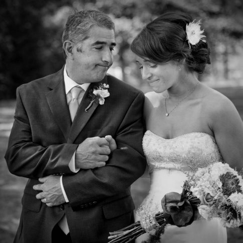 The father of the bride looks tenderly at his daughter as they prepare to proceed down the aisle.