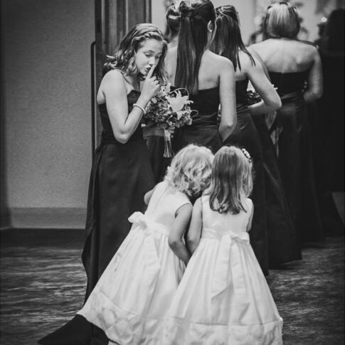 A bridesmaid looks back to gently shush two excited flower girls seconds before they proceed into the chapel.