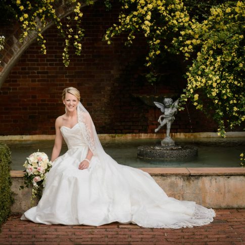 A bride smiles as she is seated on the ledge of a fountain in Furman University's Rose Garden in Greenville, SC.