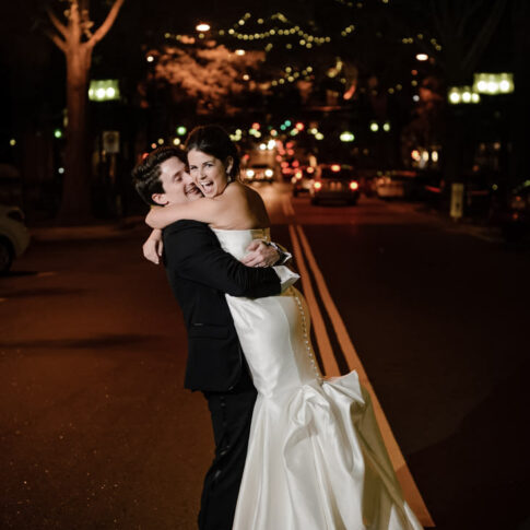 The bride looks over her shoulder as her new groom swoops her up into his arms in the middle of the street of downtown Greenville, SC.