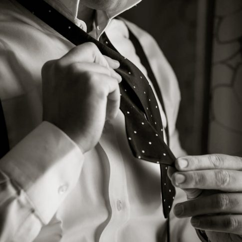 A groom takes care in tying his bowtie in preparation for his upcoming nuptials.