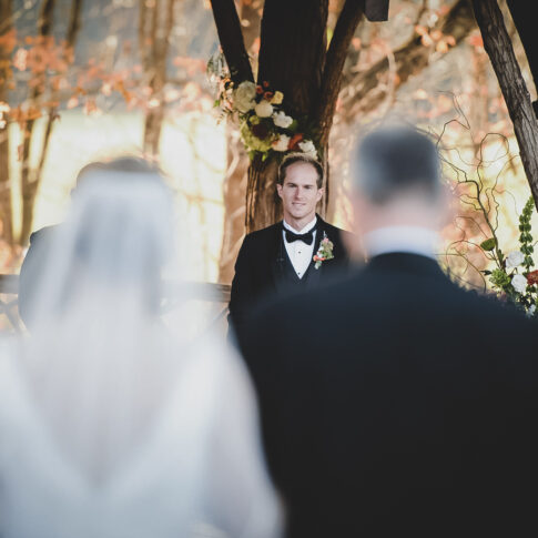 The groom smiles in anticipation as he sees his bride walking down the aisle towards him.