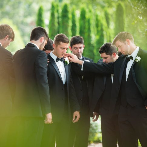 Groomsmen lay hands on the groom in prayer as they prepare for the upcoming wedding ceremony.