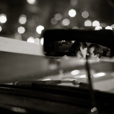 Caught in the reflection of a rearview mirror, newlyweds kiss as they depart for their honeymoon.