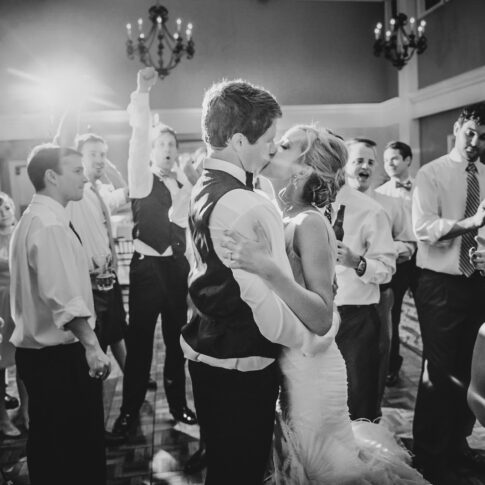 Newlyweds kiss at the end of their reception as the wedding party looks on and cheers.