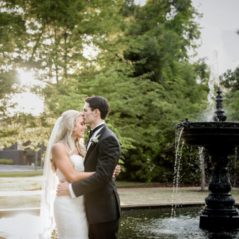 Husband kisses his new wife on the forehead beside the fountain at the Piedmont Club.