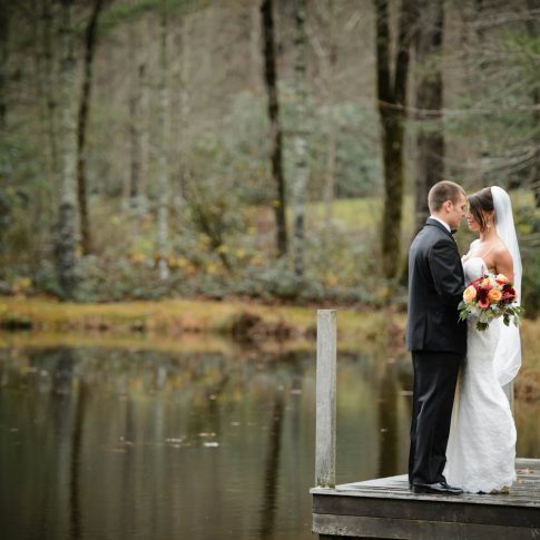 Standing on the dock overlooking the pond at Lonesome Valley in Cashiers, NC, newlyweds share a loving gaze.