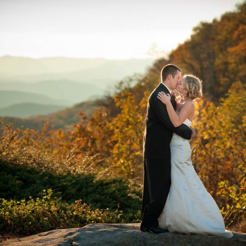 A bride and groom kiss while standing on a rock on Glassy Mountain.