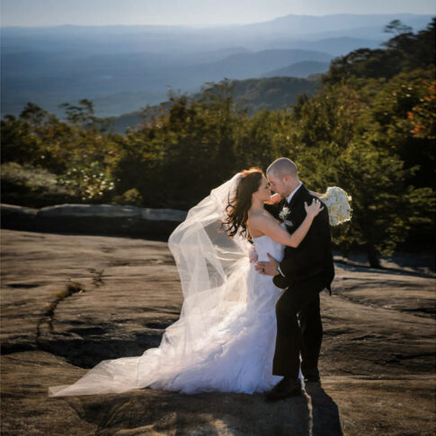 The bride and groom softly embrace as they stand on a rock overlooking the mountains at the Cliffs at Glassy.