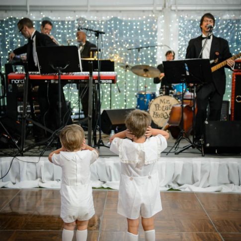 Two young boys stand on the dance floor facing the band and covering their small ears to ease the volume of the music.