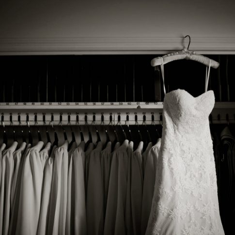 The wedding dress hangs from the moulding of a closet beside rows of choral robes.