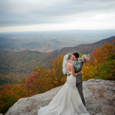 Standing on a boulder overlooking the Blue Ridge mountains outside of Symmes Chapel, newlyweds share a kiss.