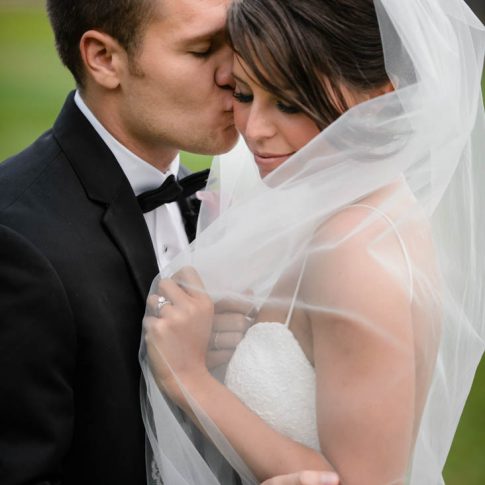 The groom softly kisses his bride on the cheek as she pulls her veil around herself.