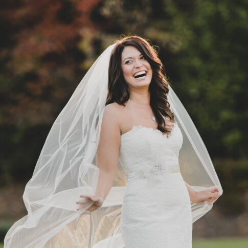 A bride laughs as she holds her veil back from the oncoming wind as she poses on the golf course of the beautiful Cliffs at Glassy Mountain.