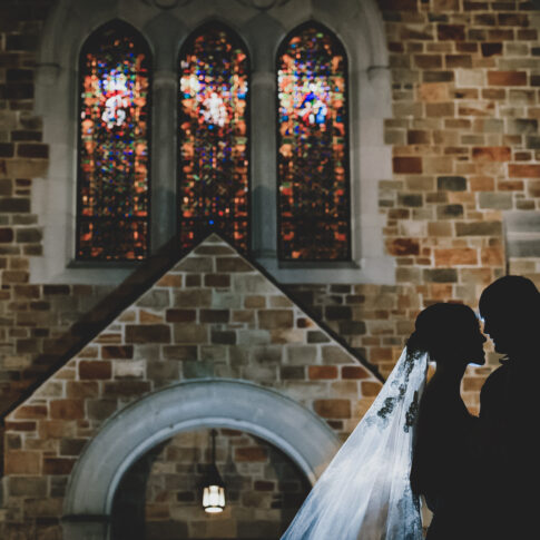 A bride and groom stand in front of a church at night.