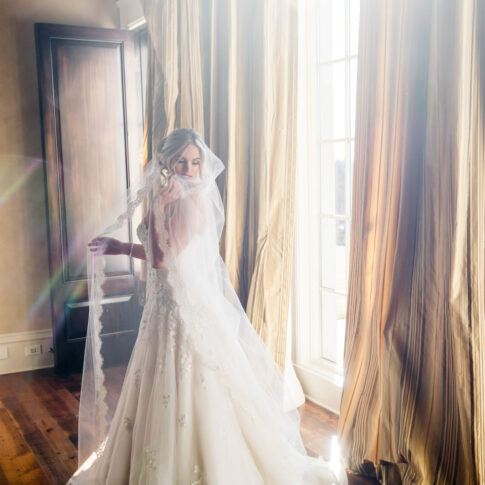 Bridal portraits of a bride standing in the sunshine streaming through the windows.