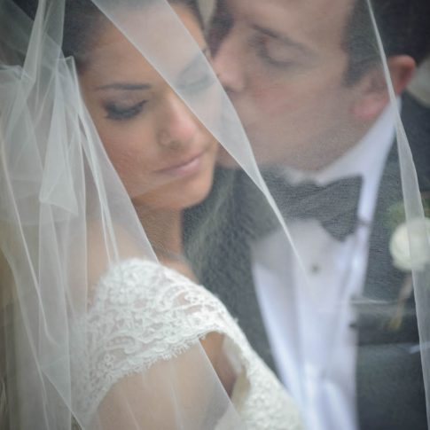 A groom softly kisses her bride underneath her veil.