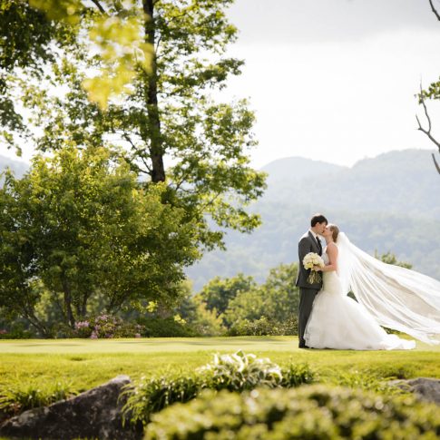 The bride and groom share a kiss surrounded by the green forestry overlooking the mountains in Cashiers, NC.