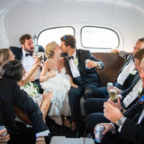 The bride and groom share a kiss amongst their celebrating wedding party en route to their reception venue.