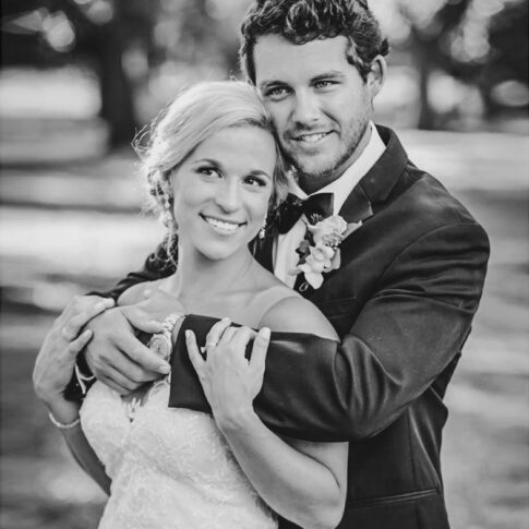 A new husband embraces his wife from behind as they smile happily.