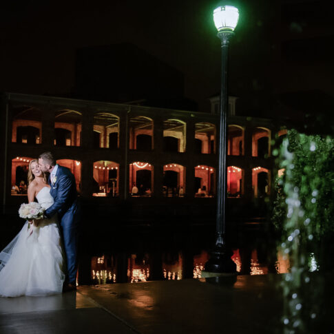 A couple shares a playful kiss outside the Wyche Pavilion while their guests enjoy their reception.